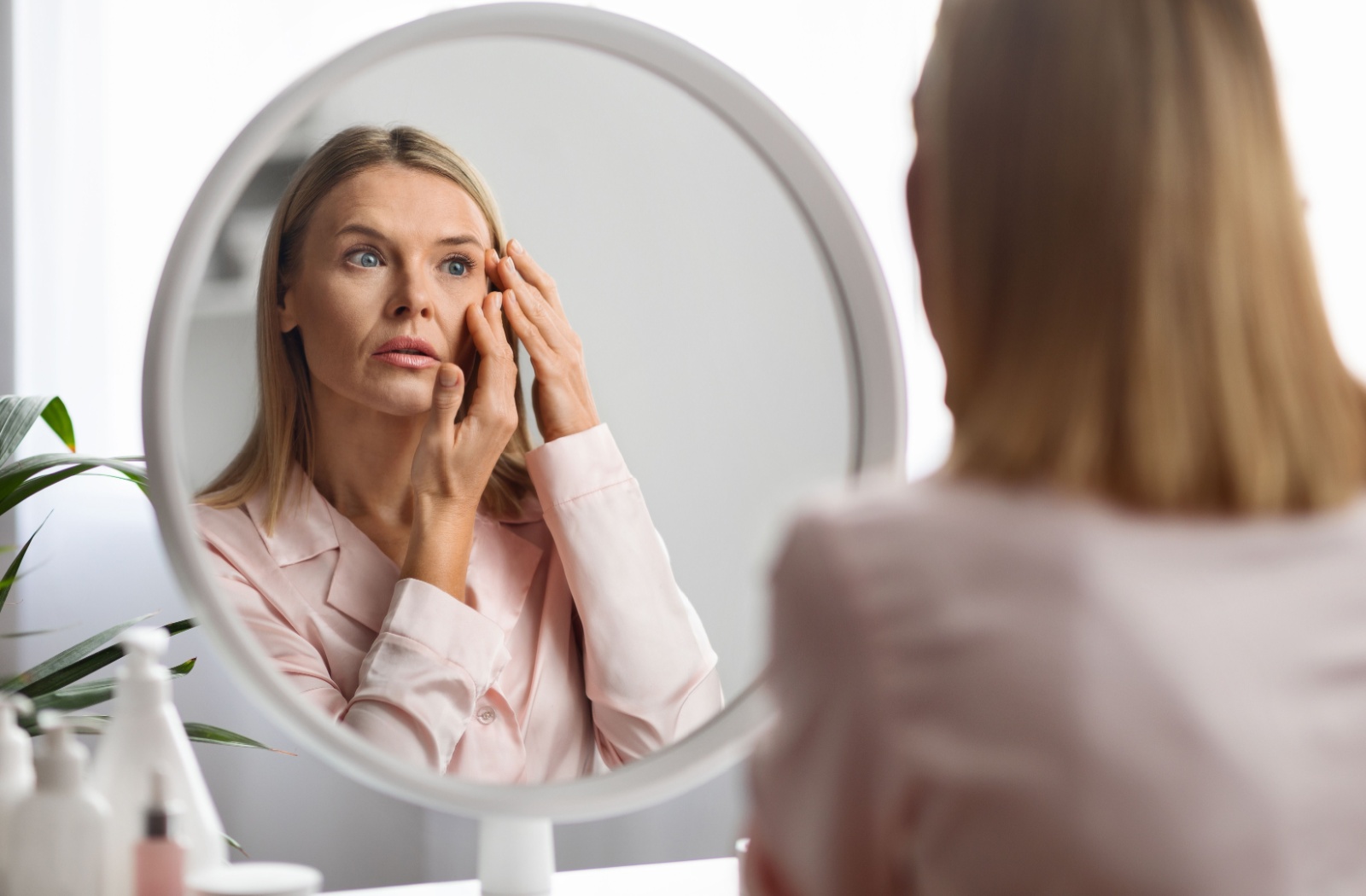 A person examines the dry skin under their eyes in a mirror.