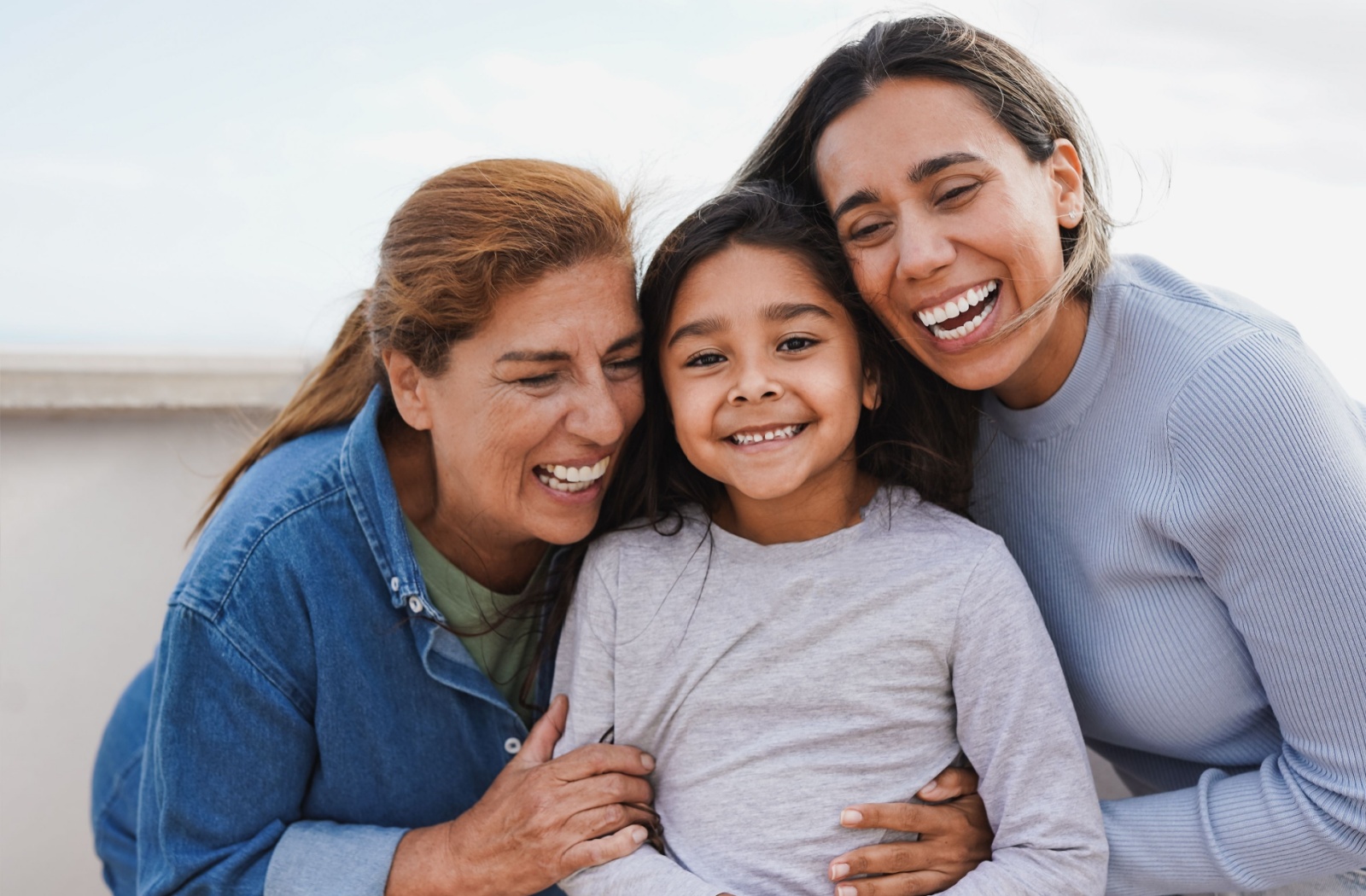 Three generations of a family smiling and laughing together, with the youngest sandwiched between the older two