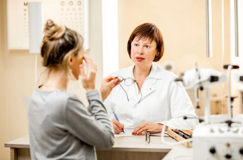 A young optometrist holding a pair of glasses in one hand and a contact lens case in the other.