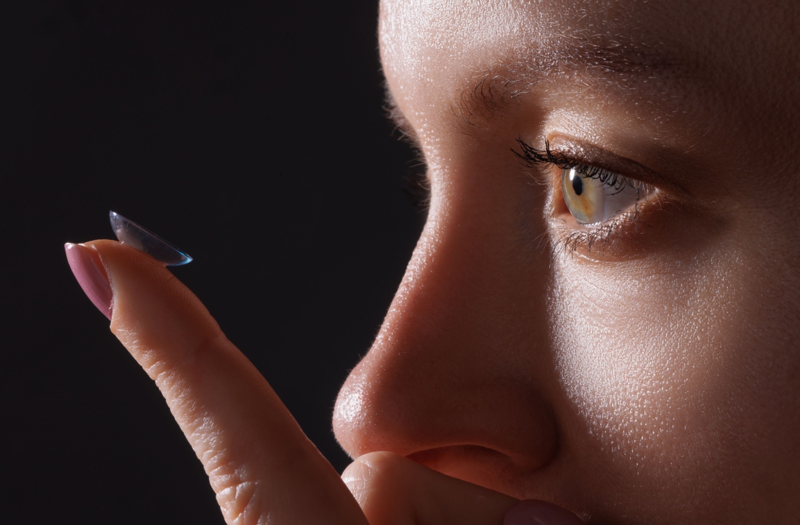 A person stares at a contact lens balanced on their index finger.