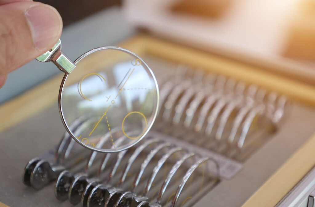 Close-up of a hand holding a progressive eyeglass lens with measurement markings above a tray of trial lenses used for fitting and testing.