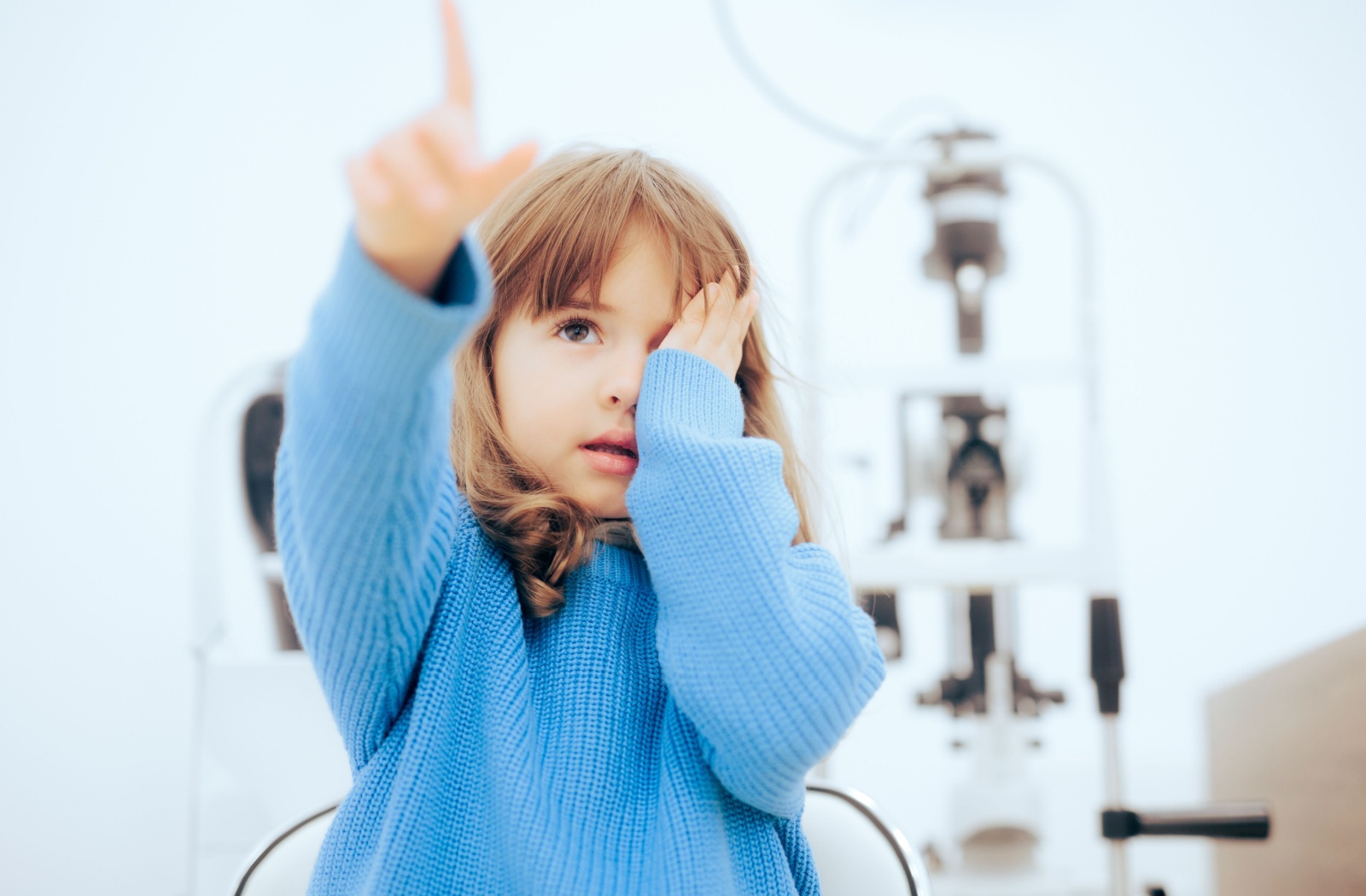 A young child covering one eye and pointing forward during a vision test at an optometry clinic, illustrating pediatric eye exams.