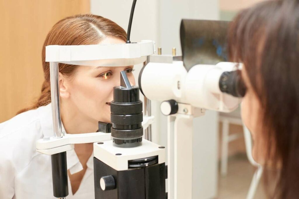 Female optometrist examining patient's eye using slit lamp microscope during comprehensive contact lens fitting exam in clinical setting.
