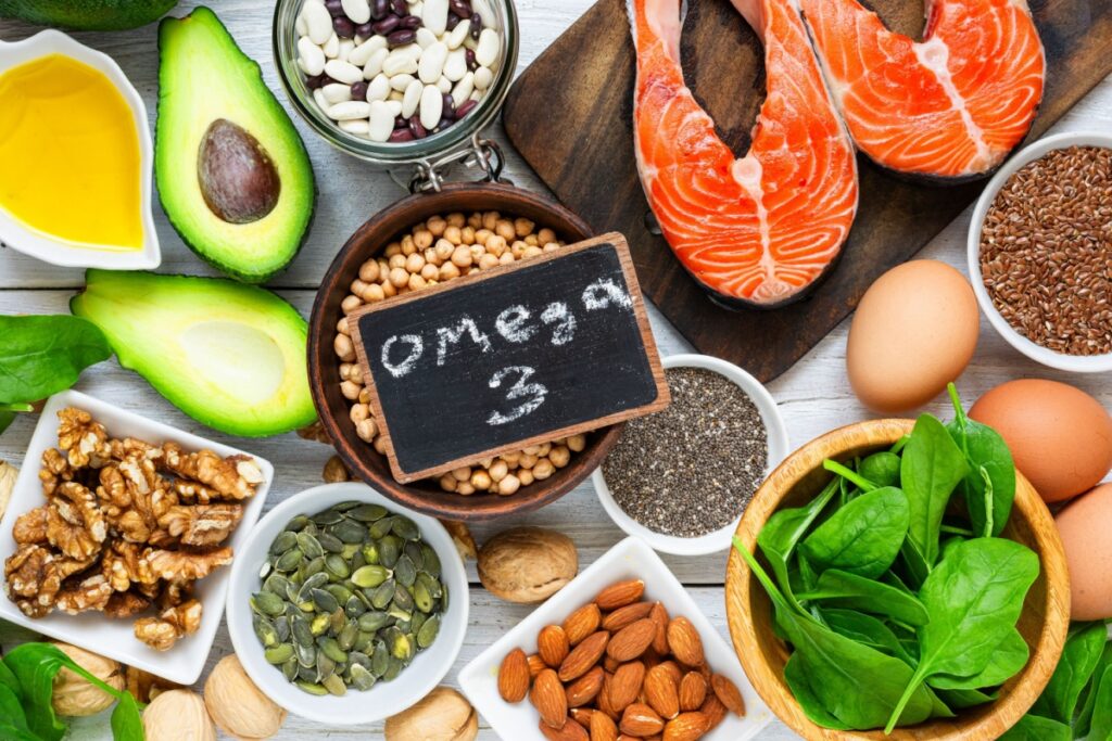Various healthy fat foods surrounding a chalkboard sign that says "Omega 3".