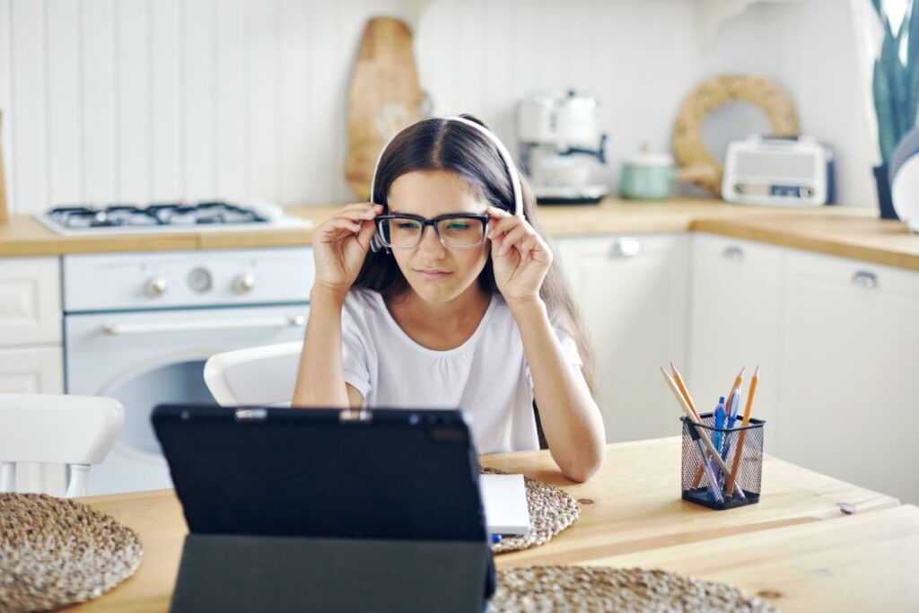 Teen girl doing homework while holding her glasses on her face.